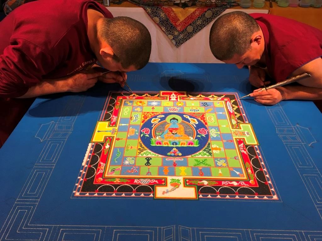 Two Tibetan monks create an intricate sand mandala. Courtesy of Norman Cultural Connections.